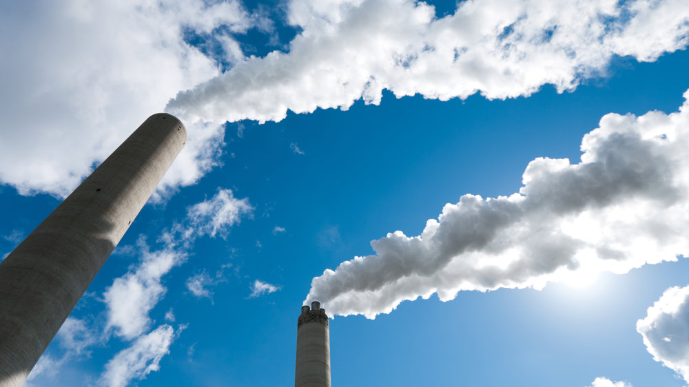 Large chimneys puffing out clouds of pollutants into the air with blue sky 