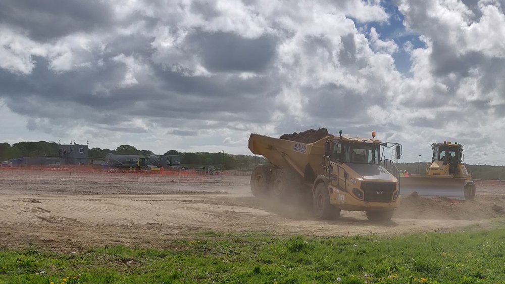 Two large building site vehicles collecting rubble with clouds overhead